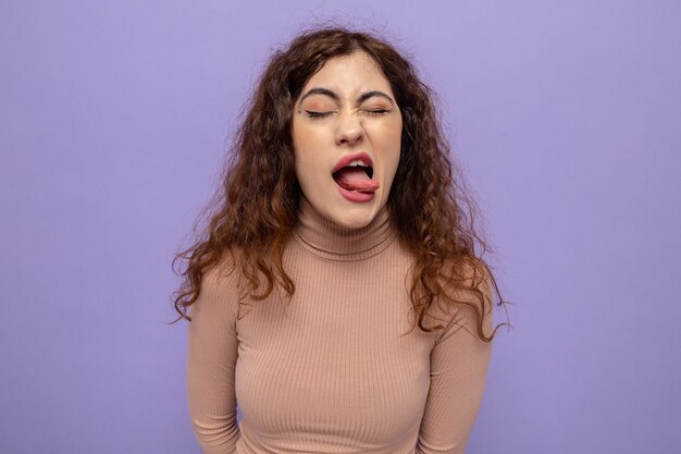 Happy and joyful young beautiful woman in beige turtleneck sticking out tongue