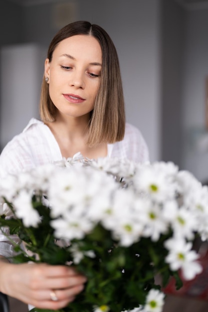 Happy and joyful young woman in white arranging white flowers at home in the kitchen