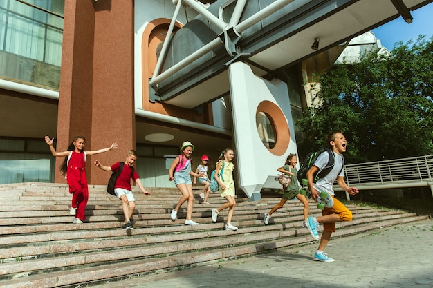 Happy kids playing at city's street in sunny summer's day in front of modern building. Group of happy childrens or teenagers having fun together. Concept of friendship, childhood, summer, holidays.