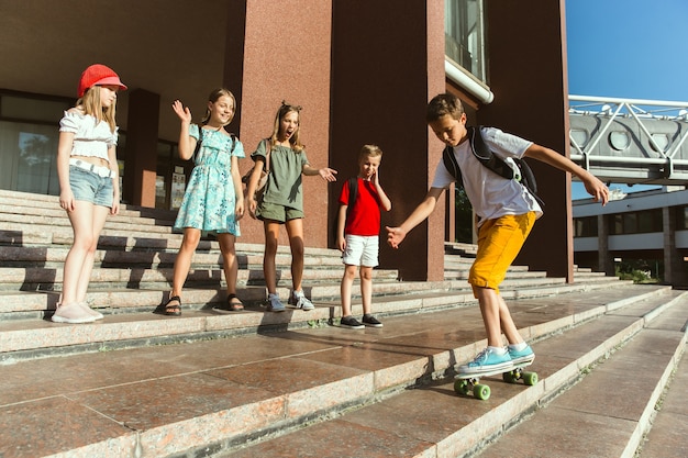 Happy kids playing at city's street in sunny summer's day in front of modern building. Group of happy childrens or teenagers having fun together. Concept of friendship, childhood, summer, holidays.