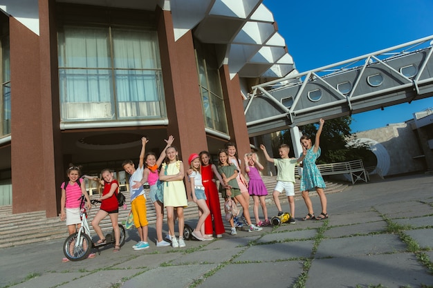 Free photo happy kids playing at city's street in sunny summer's day in front of modern building. group of happy childrens or teenagers having fun together. concept of friendship, childhood, summer, holidays.