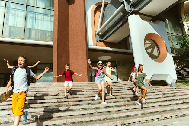 Free Photo happy kids playing at city's street in sunny summer's day in front of modern building. group of happy childrens or teenagers having fun together. concept of friendship, childhood, summer, holidays.