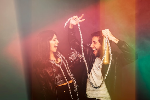 Free photo happy lady and guy with tinsel and bottle of beverage showing two gesture