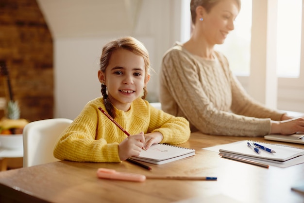 Free photo happy little girl drawing while her mother is working on laptop at home