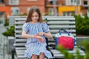 Free photo happy little girl sitting and using her kid smart watch near school.