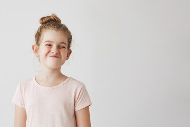 Free Photo happy little girl with blond long hair in bun hairstyle funny smiling with losed eyes, making silly faces on school photoshoot.