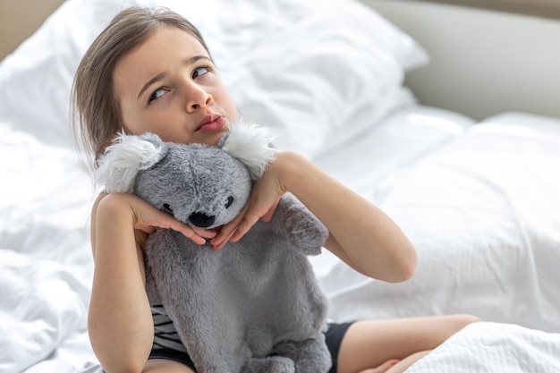 Free photo happy little girl with soft toy koala in bed