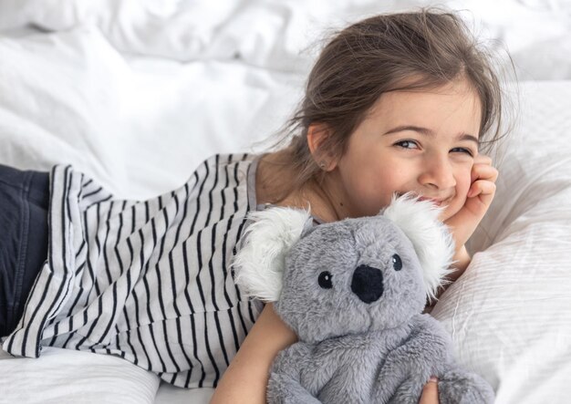 Happy little girl with soft toy koala in bed