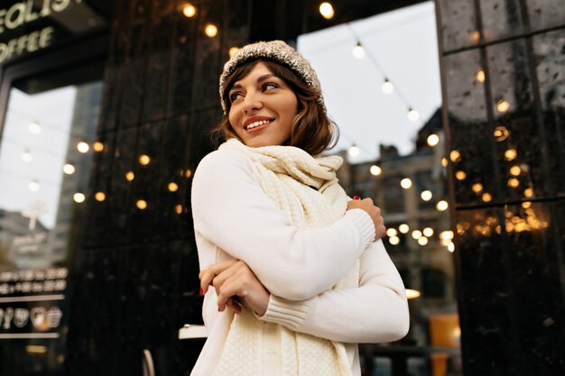 Happy lovable woman in white winter outfit walking on the street with happy smile on background with christmas lights High quality photo