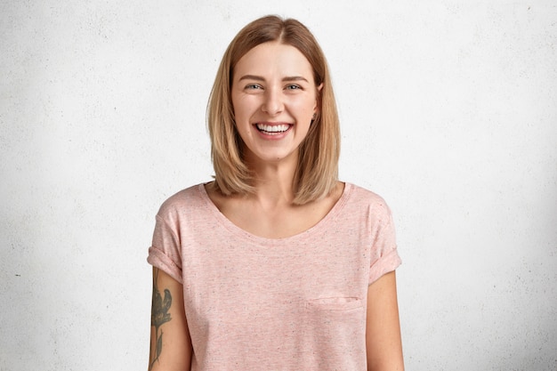 Free photo happy lovely pretty young female model with bobbed hairstyle and shining smile, being in good mood after successful shopping, dressed in casual loose t shirt