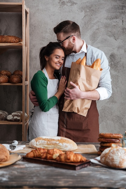 Happy loving couple bakers standing near bread and hugging