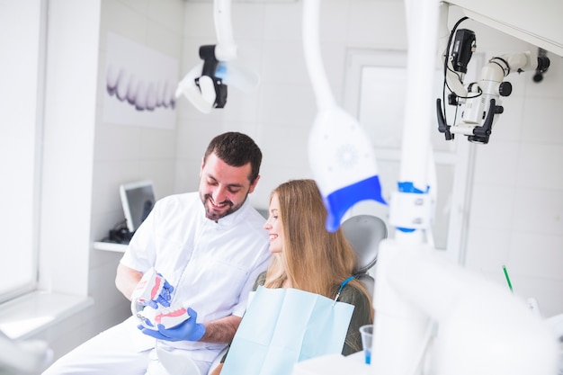 Happy male dentist showing teeth model to patient