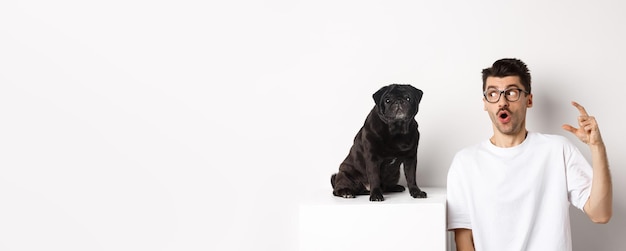 Free Photo happy male dog owner sitting near cute black pug looking at pet with amazed and surprised face white