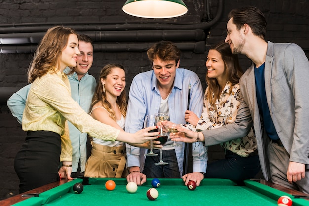 Free photo happy male and female friends toasting wine in club over snooker table in club