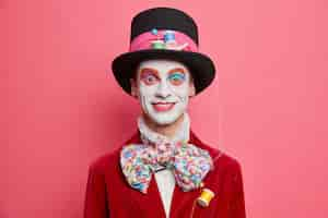 Free photo happy male hatter with colorful makeup dresses for halloween party has image of fictional character from wonderland poses against vivid rosy studio wall