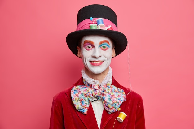 Free Photo happy male hatter with colorful makeup dresses for halloween party has image of fictional character from wonderland poses against vivid rosy studio wall