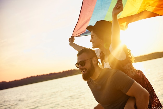 Free Photo happy man carrying woman with rainbow flag by sea