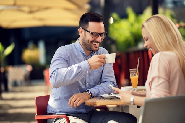 Happy man drinking coffee and having fun with his girlfriend while she is using cell phone in a cafe