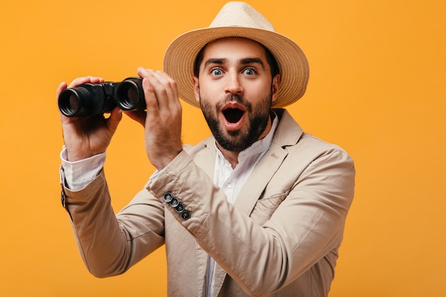 Happy man in hat and beige suit holding binoculars