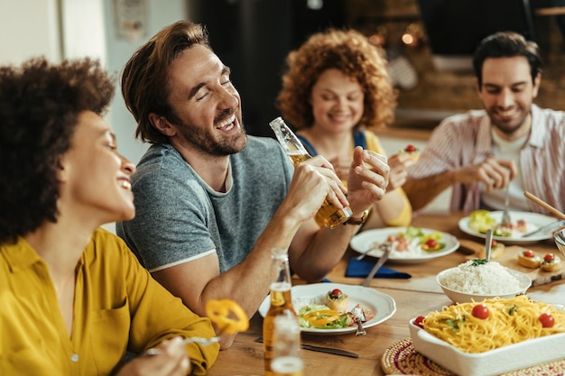 Happy man having fun while having lunch and drinking beer with friends at home