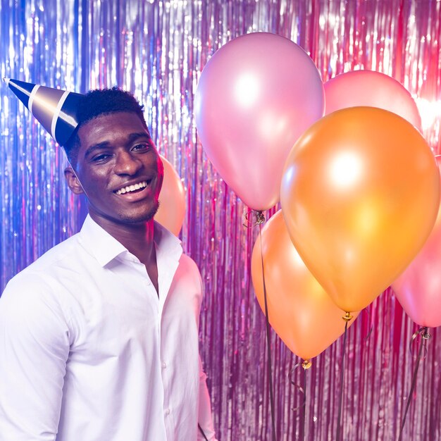 Happy man holding balloons front view and wearing party hat