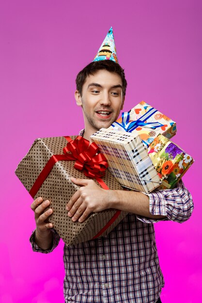 Happy man holding birthday gifts in boxes over purple wall.