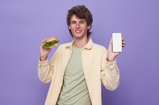 Free photo happy man holding hamburger and showing food delivery app on mobile phone to order lunch