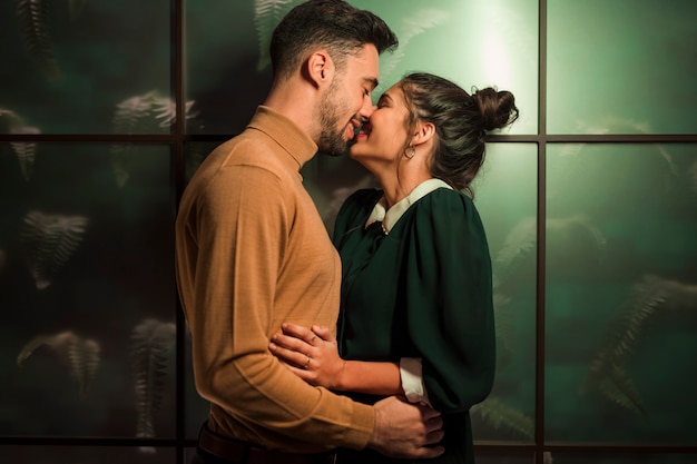 Happy man kissing cheerful woman near wall