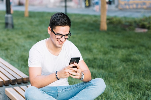 Happy man sitting on bench using cellphone