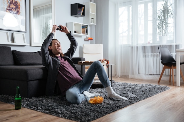 Happy man sitting at home indoors play games with joystick