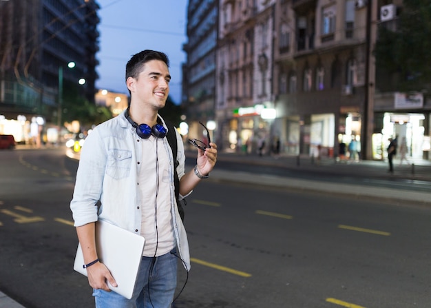 Happy man standing on roadside holding laptop