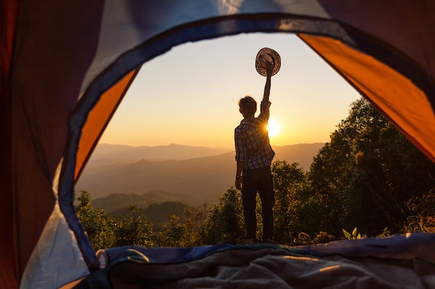 Happy man stay near tent around mountains under sunset light sky enjoying the leisure and freedom.