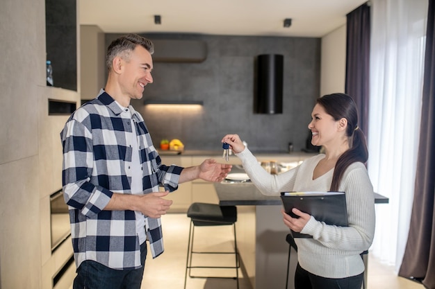 Free photo happy man taking keys from realtor woman standing indoors