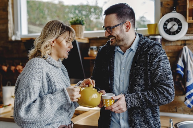 Free photo happy man talking to his wife while she is pouring him a cup of tea in the kitchen