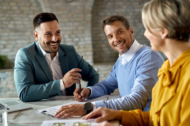 Happy man talking to his wife while signing an agreement with insurance agent in the office