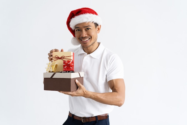 Happy man wearing Santa hat and showing gift boxes