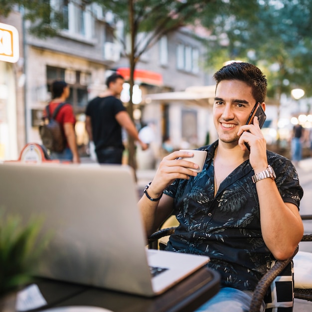 Happy man with cup of coffee talking on cellphone