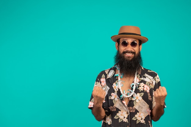 Free photo the  of a happy man with a long beard wearing a hat, wearing a striped shirt showing a gesture on a blue .