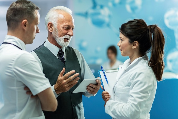 Free photo happy mature businessman using digital tablet while talking to healthcare workers in a hallway at clinic