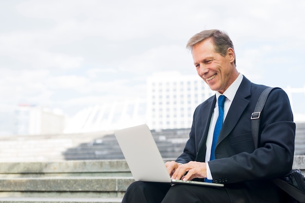 Free photo happy mature businessman working on laptop at outdoors