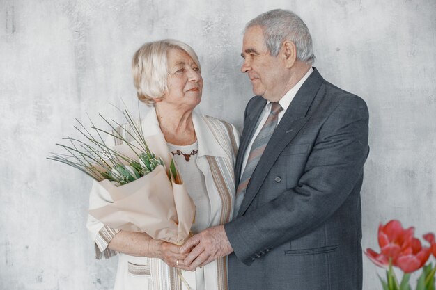 Happy mature couple in love embracing,  grey haired husband and wife. Senior woman holding a bunch of flowers.