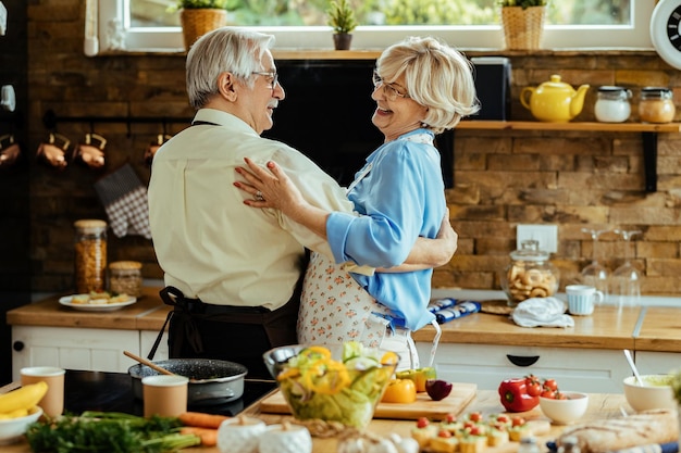 Happy mature husband and wife having fun while dancing in the kitchen