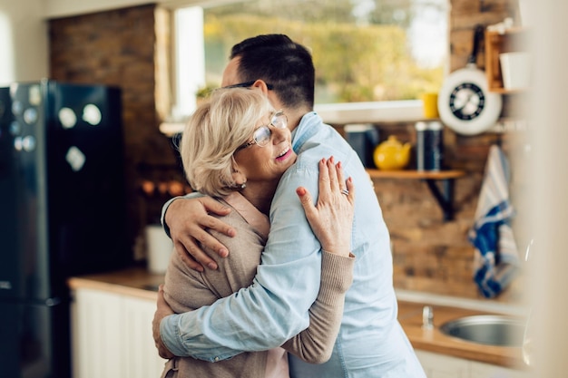 Happy mature woman and her adult son embracing in the kitchen