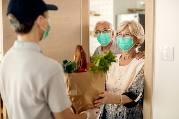 Happy mature woman and her husband receiving groceries at home during coronavirus epidemic