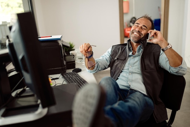 Happy mechanic making a phone call while relaxing in the office of a repair shop