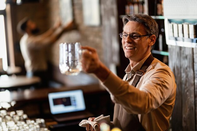 Happy mid adult barista cleaning drinking glass after working hours in a pub