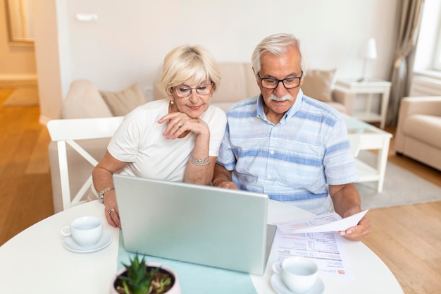 Free photo happy middle aged husband and wife sitting at table with laptop and paper bills calculating domestic incomes together at home