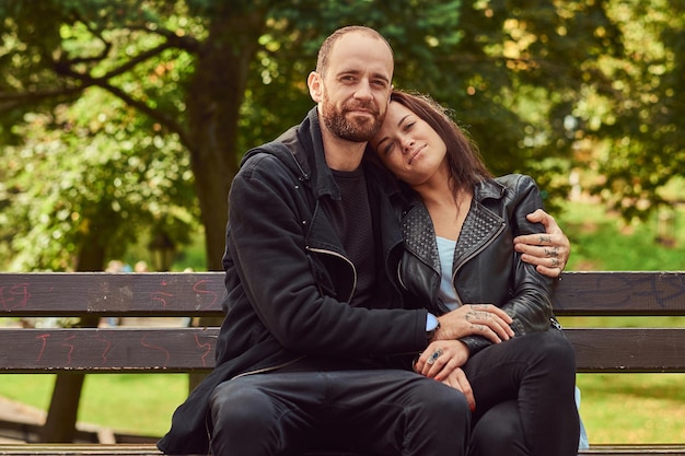 Free photo happy modern couple cuddling on a bench in the park. enjoying their love and nature.