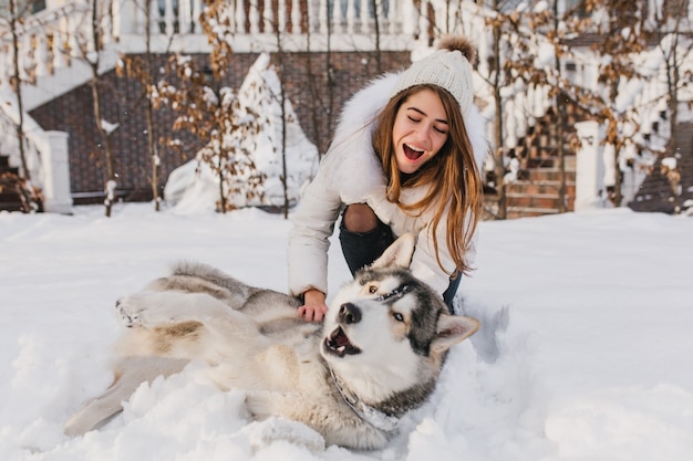 Free Photo happy moments on winter time of amazing youful woman playing with husky dog in snow. brightful  positive emotions, true friendship, pets love, best friends, smiling, having fun, winter holidays.