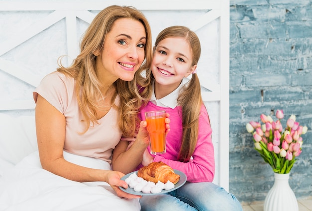 Happy mother and daughter sitting with croissant on bed